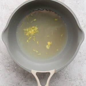A gray saucepan filled with water and small yellow floral bits on a textured light gray surface.