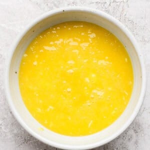 A white bowl filled with beaten eggs on a textured white surface.