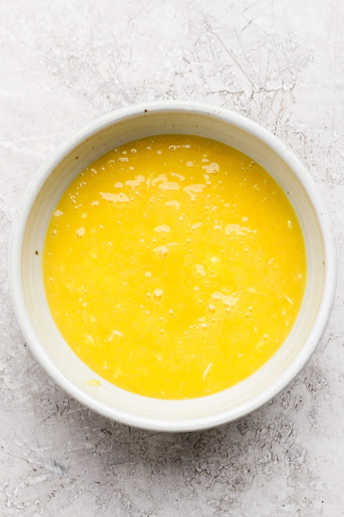 A white bowl filled with beaten eggs on a textured white surface.