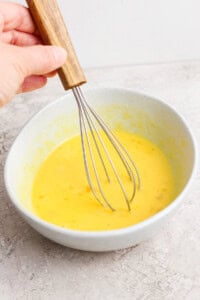 Hand whisking yellow batter in a gray bowl.