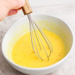 Hand whisking yellow batter in a gray bowl.