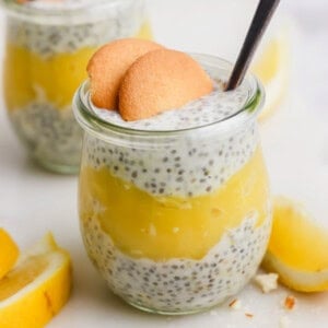 Glass jar filled with chia seed pudding and lemon layer, topped with two cookies and a spoon. Lemon slices are in the background.