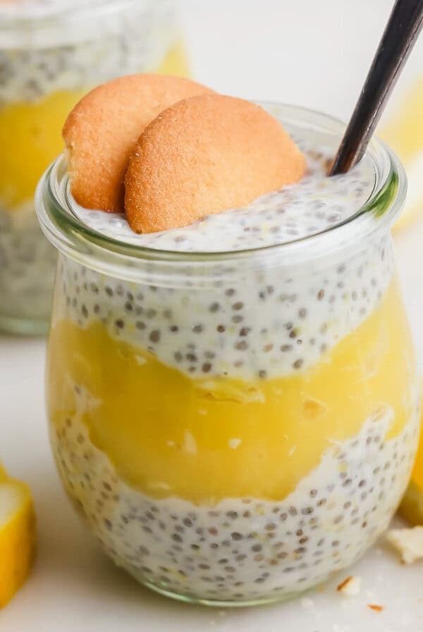 Glass jar filled with chia seed pudding and lemon layer, topped with two cookies and a spoon. Lemon slices are in the background.