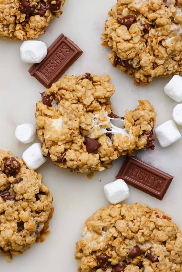 Oatmeal cookies with chocolate chips and melted marshmallows, surrounded by mini marshmallows and chocolate chunks on a marble surface.
