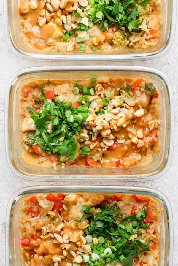 Three glass containers filled with a delicious dish featuring rice, diced vegetables, chopped nuts, and tender peanut chicken, all garnished with fresh herbs and green onions.