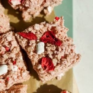 Rice crispy treat square with red dried strawberries and small marshmallows on a green and beige surface.