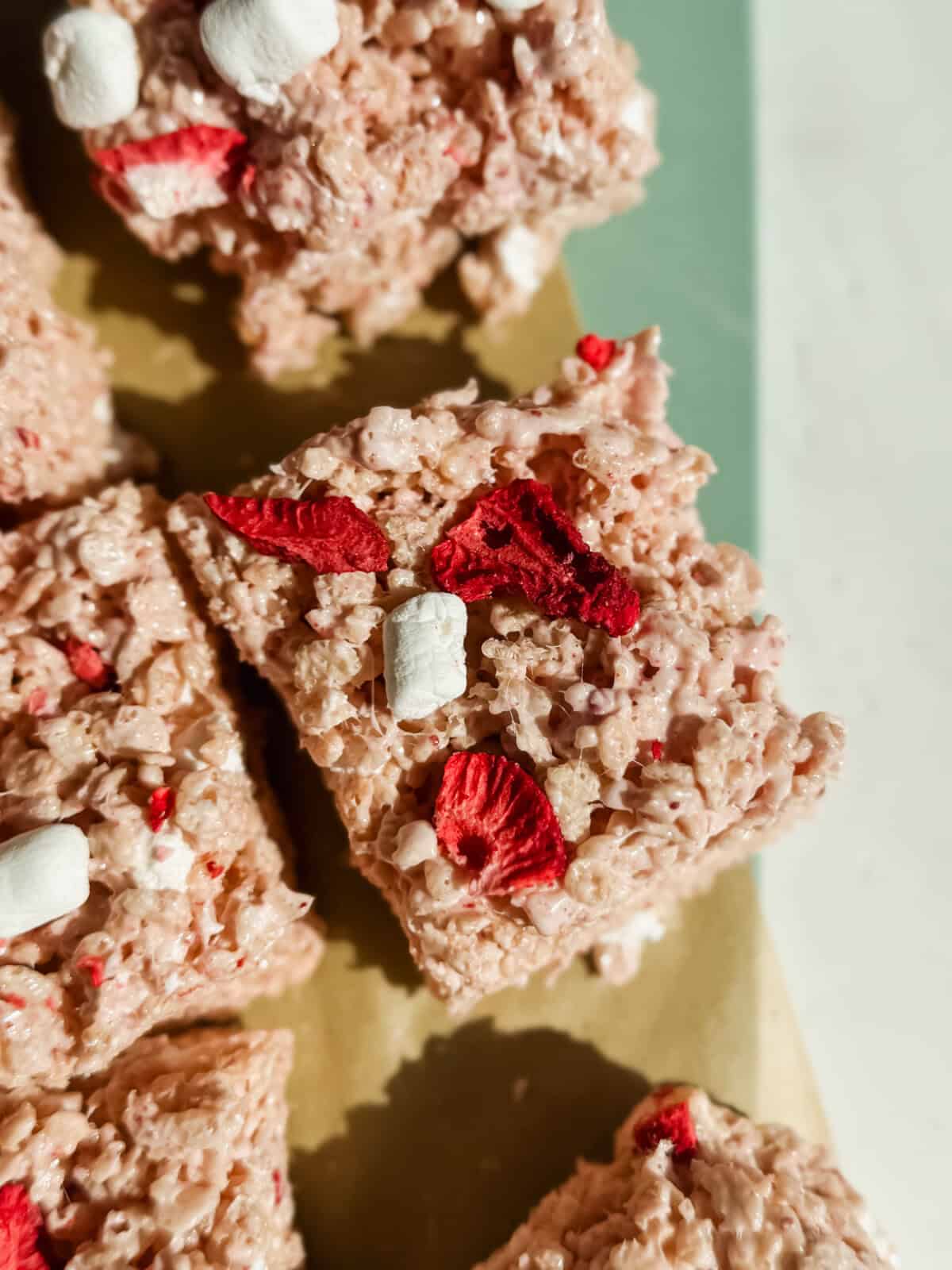 Close-up of cereal treats with red dried fruit pieces and small marshmallows on a light surface.