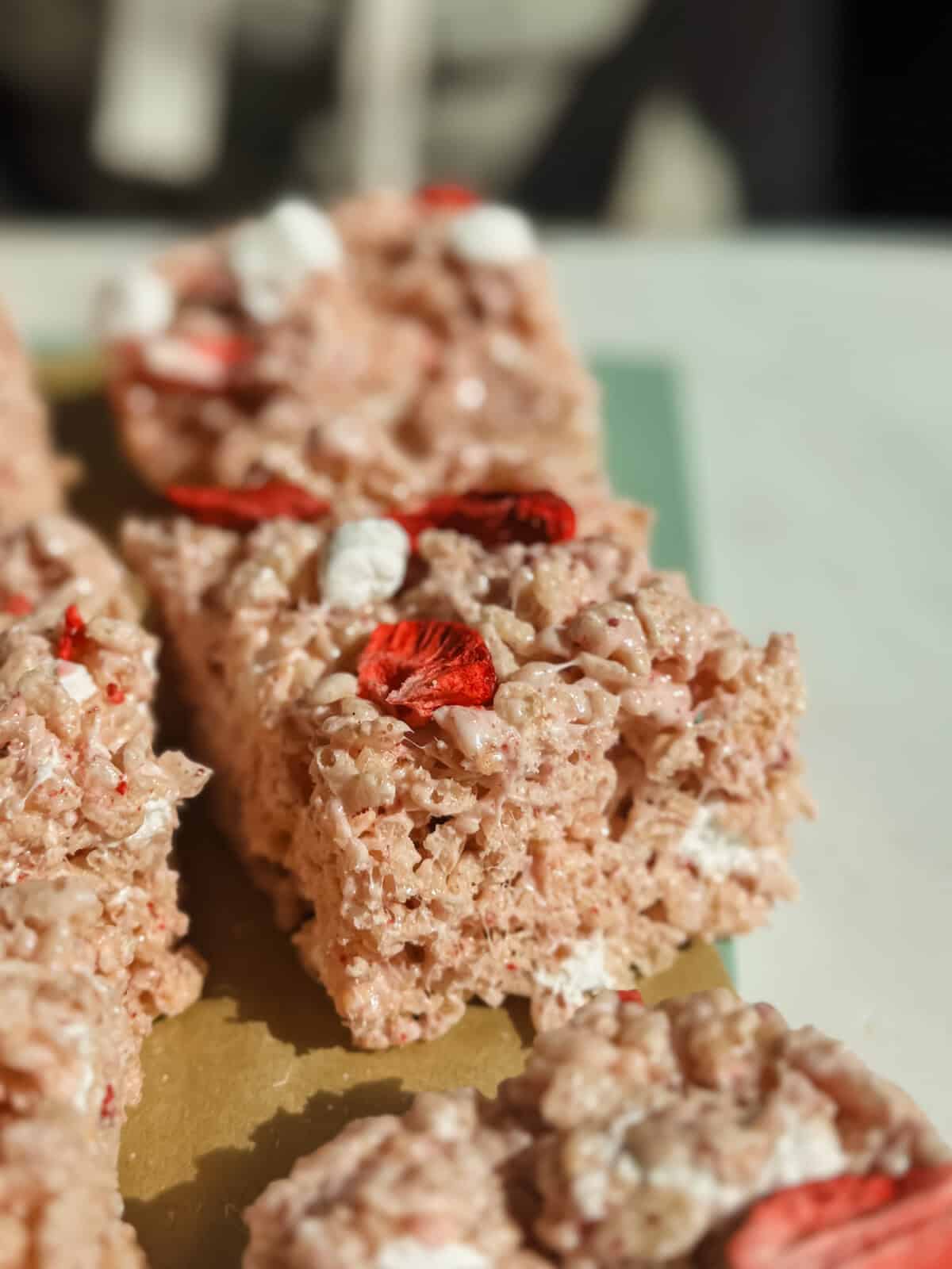 Close-up of rice crispy treats with marshmallows and dried strawberry slices on top, arranged on a cutting board.