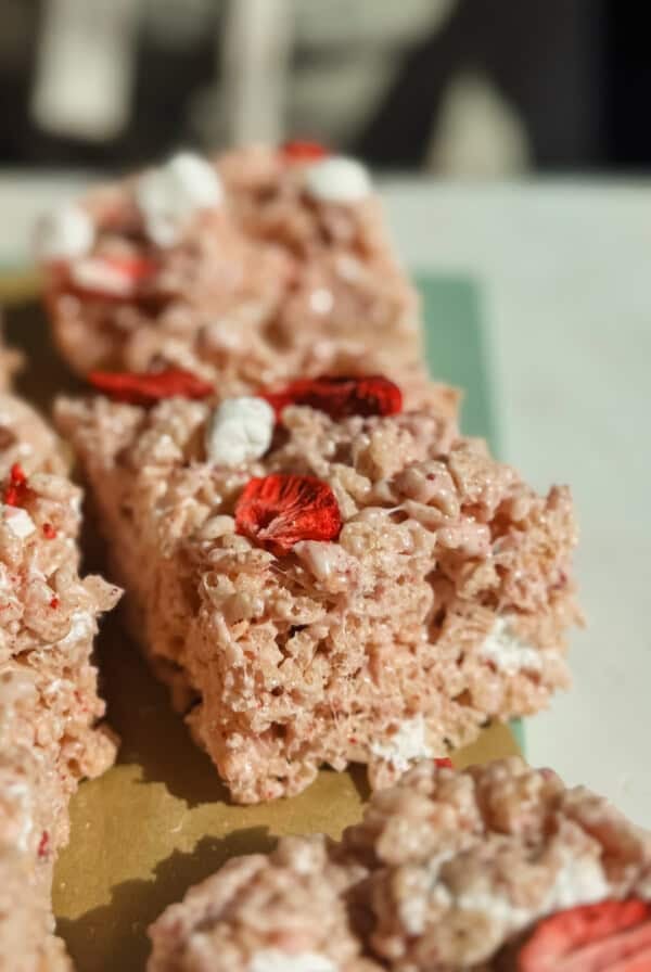 Close-up of rice crispy treats with marshmallows and dried strawberry slices on top, arranged on a cutting board.