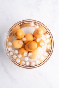 A bowl of brown eggs is submerged in water with ice cubes, set against a white background.