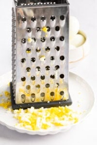 A metal cheese grater on a white plate with finely grated egg, alongside a bowl containing whole boiled eggs.
