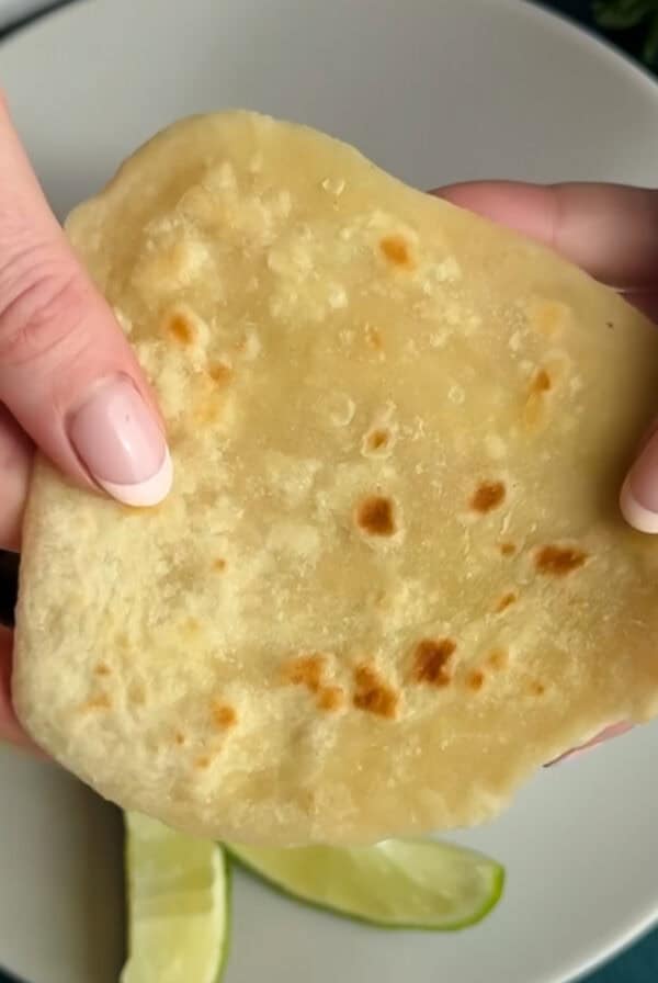 Two hands hold a flatbread over a plate containing lime wedges.