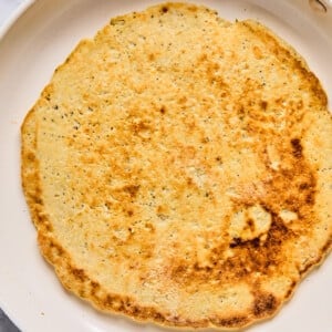 A cooked flatbread with a golden-brown surface sits in a white skillet on a marble countertop.