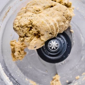 A close-up view of dough formed into a ball inside a food processor with a visible metal blade.