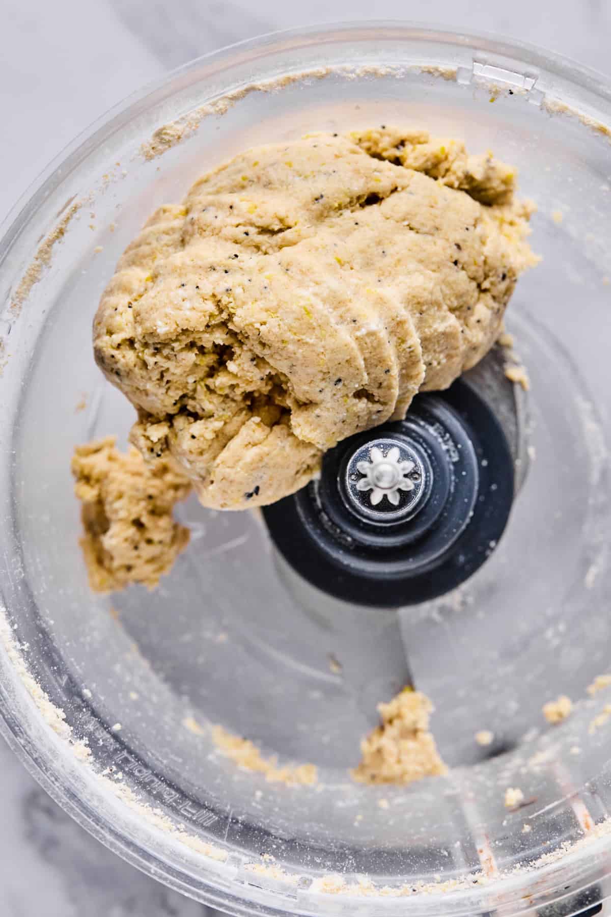 A close-up view of dough formed into a ball inside a food processor with a visible metal blade.