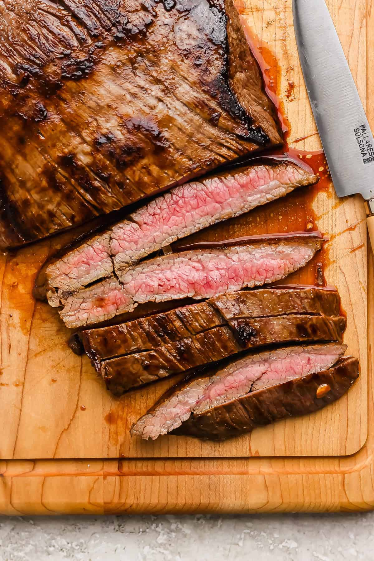 Sliced medium-rare steak on a wooden cutting board with a knife beside it.