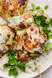 Grilled chicken skewers with a creamy sauce served over white rice and garnished with fresh cilantro.
