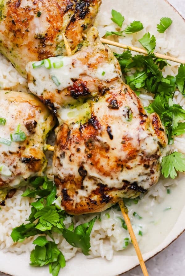 Grilled chicken skewers with a creamy sauce served over white rice and garnished with fresh cilantro.