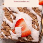 A slice of baked oatmeal topped with icing and a strawberry slice sits on a speckled plate with a whole strawberry and a fork.