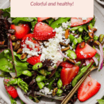 A salad with strawberries, pistachios, red onion, feta cheese, and greens served on a white plate with a fork. A text overlay reads "Honey Pistachio Summer Salad: Colorful and healthy!.