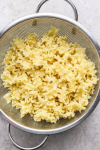 Cooked mafaldine pasta is draining in a metal colander set on a light-colored surface.