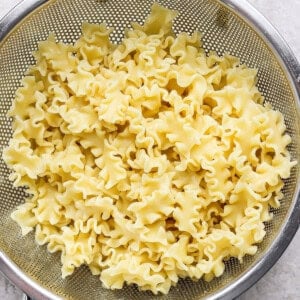 Cooked mafaldine pasta is draining in a metal colander set on a light-colored surface.