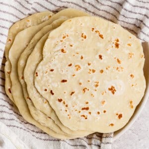 A stack of homemade flour tortillas rests on a striped kitchen towel.