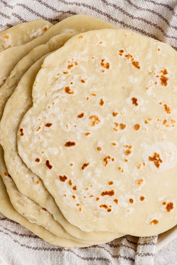 A stack of homemade flour tortillas rests on a striped kitchen towel.