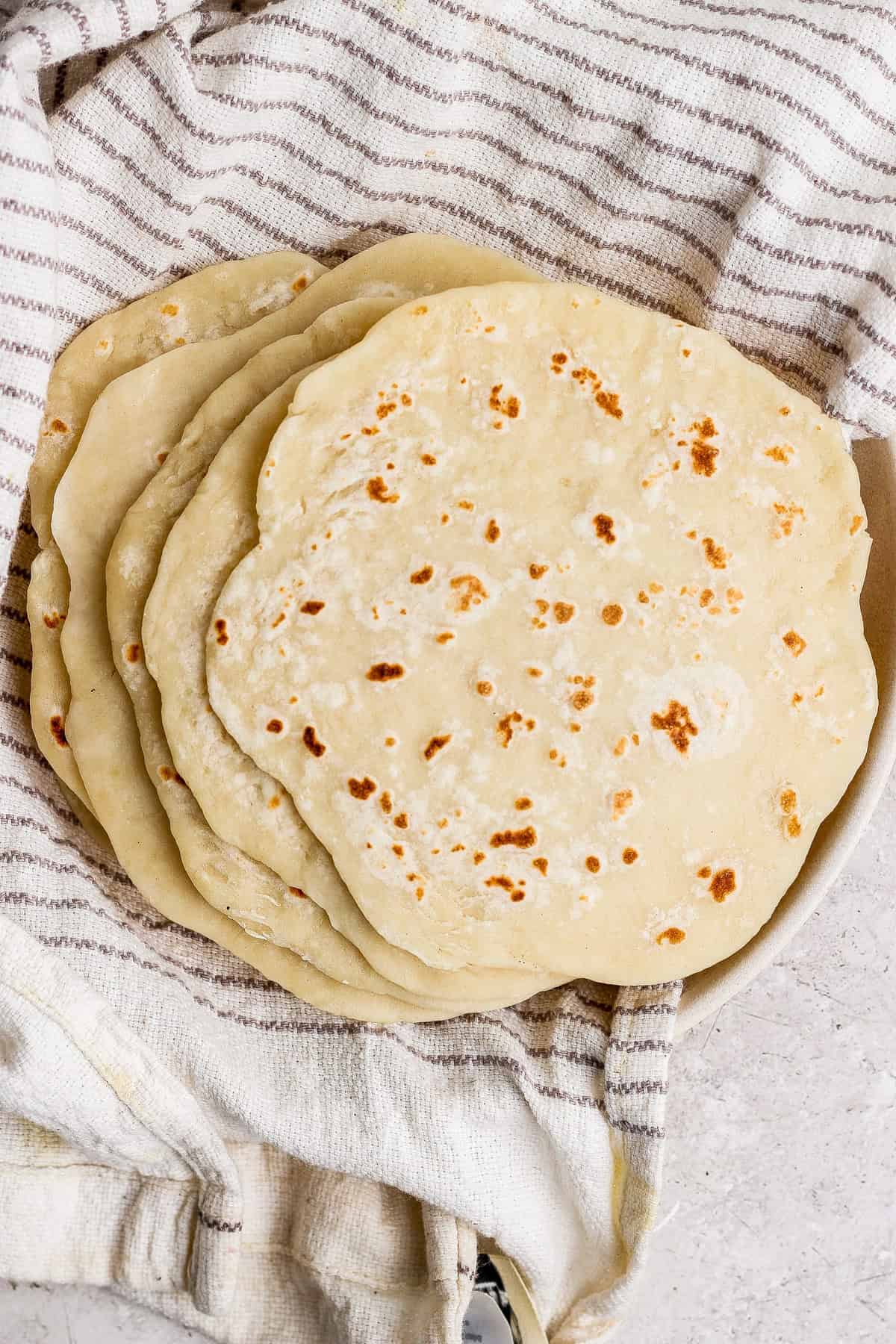 A stack of homemade flatbreads resting on a striped kitchen towel.