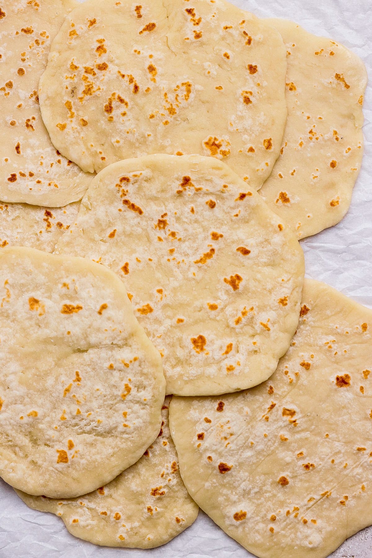 Several pieces of flatbread, slightly browned and overlapping, are laid out on a crumpled white surface.
