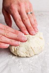Hands kneading a ball of dough on a floured surface.