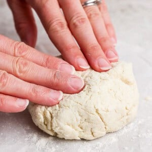 Hands kneading a ball of dough on a floured surface.