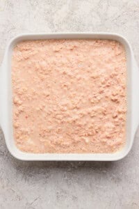 A white rectangular dish filled with an uncooked, pinkish oatmeal mixture on a textured, light-colored surface.