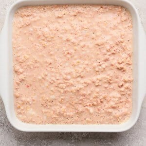A white rectangular dish filled with an uncooked, pinkish oatmeal mixture on a textured, light-colored surface.
