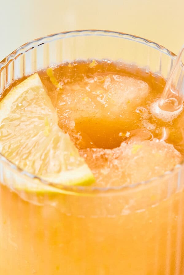 A close-up of an iced beverage in a ribbed glass, garnished with a lime wedge and served with a clear straw.