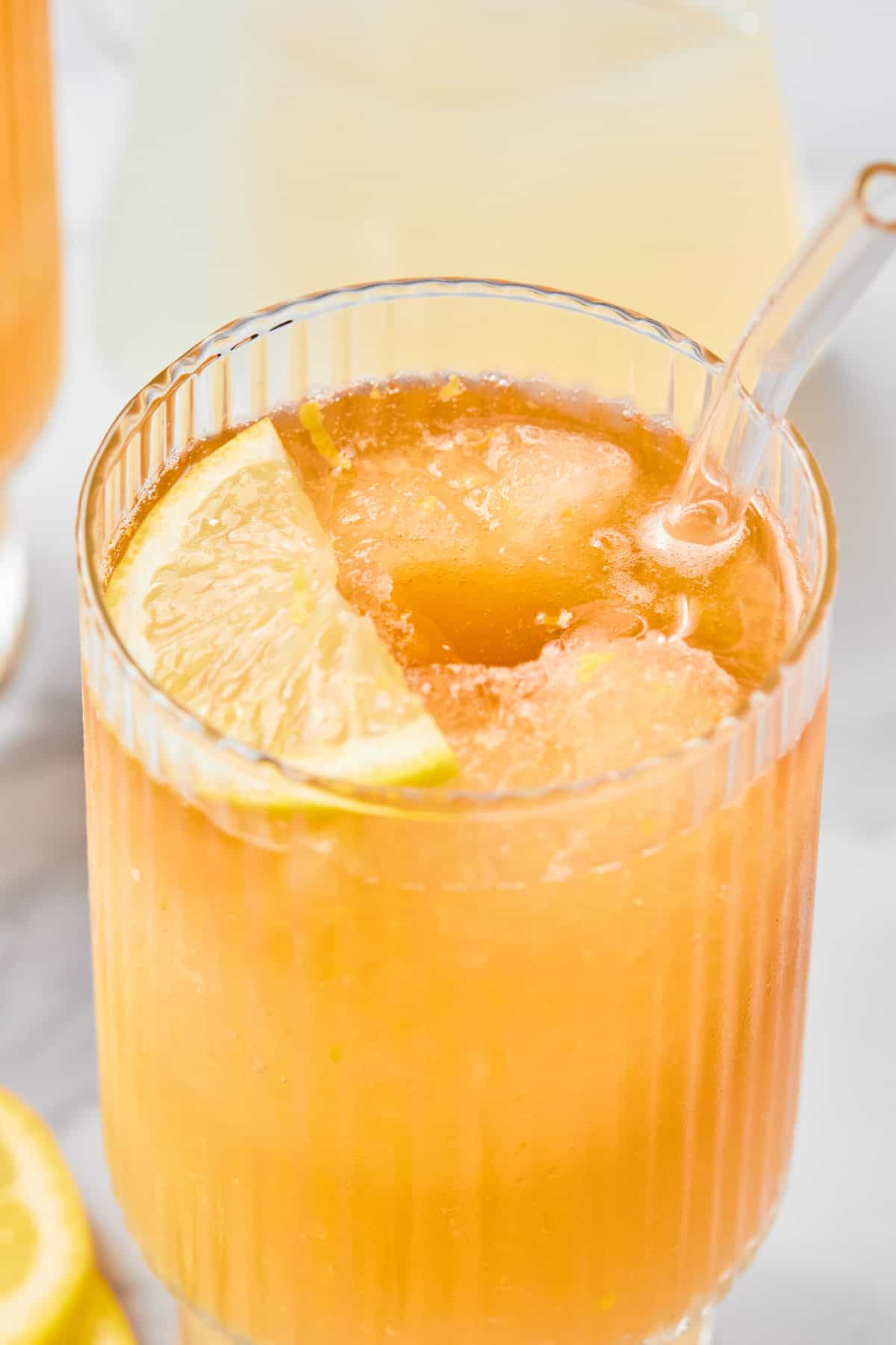 A close-up of an iced orange drink in a ribbed glass with a clear straw and a lemon slice garnish.