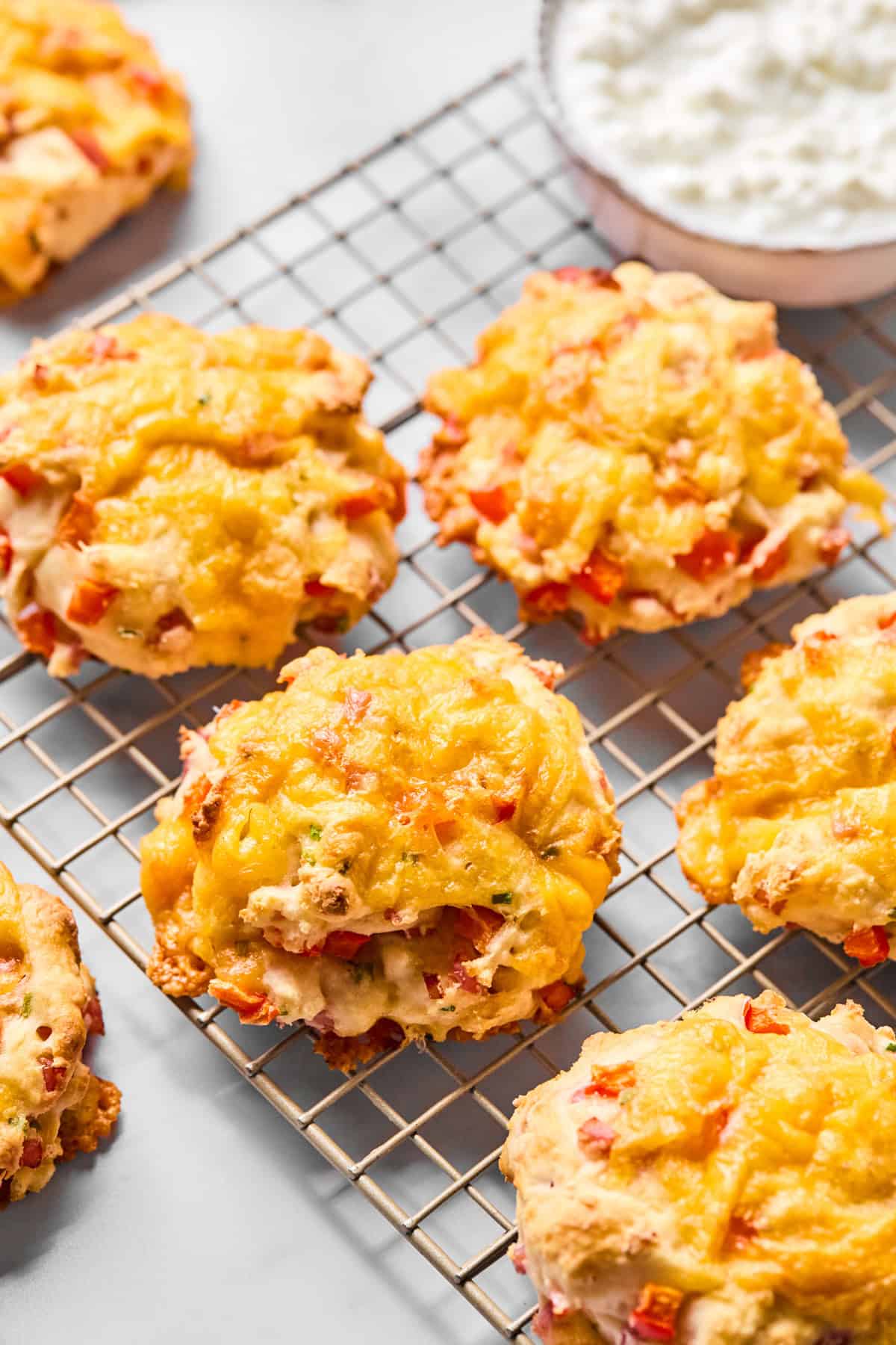 Cheddar and red pepper scones cooling on a wire rack, with a bowl of cottage cheese in the background.