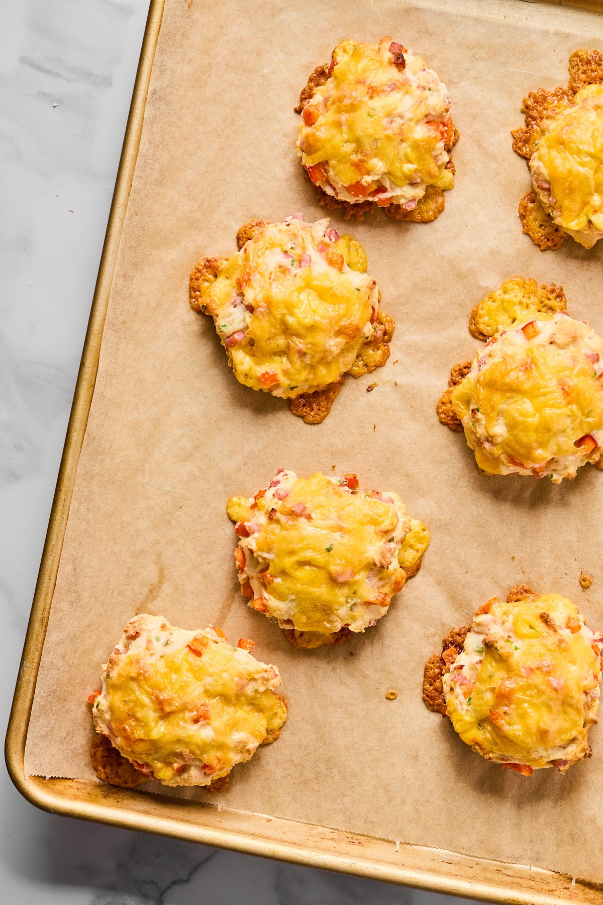 A baking sheet lined with parchment paper holds seven baked savory cheese and vegetable biscuits.