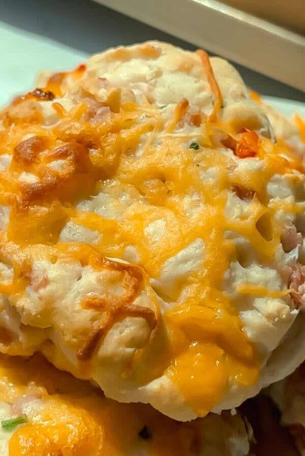 A close-up of cheesy baked biscuits with melted cheddar cheese on top, served on a white plate.