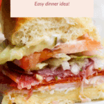 A close-up of a Hawaiian bun slider filled with deli meats, cheese, tomato, pickles, and lettuce on a white plate. Text overlay reads: “Hawaiian Bun Grinder Sliders Easy dinner idea!”.