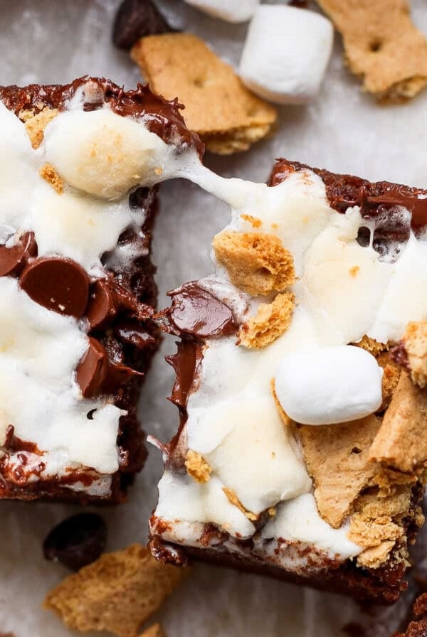 Two s'mores brownies topped with melted marshmallows, chocolate chips, and graham cracker pieces on a light background.