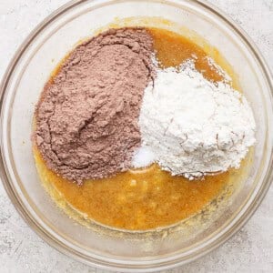 A glass bowl holds a mixture of wet ingredients, with piles of cocoa powder and flour on top, ready to be mixed for delicious s'mores brownies.