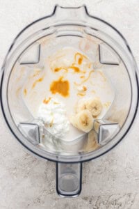 A blender containing milk, sliced banana, cottage cheese, and a drizzle of honey, viewed from above.