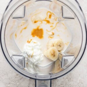A blender containing milk, sliced banana, cottage cheese, and a drizzle of honey, viewed from above.