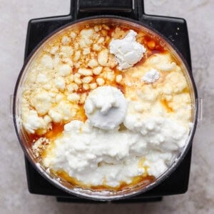 A food processor bowl filled with cottage cheese, eggs, flour, and vanilla extract, viewed from above.