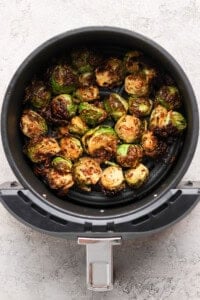 Halved Brussels sprouts cooked in an air fryer basket, showing a browned, crispy texture on a light gray countertop.