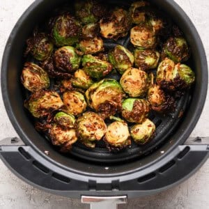 Halved Brussels sprouts cooked in an air fryer basket, showing a browned, crispy texture on a light gray countertop.