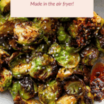 A bowl of air-fried Brussels sprouts topped with chili crisp sauce and sesame seeds, with a hand holding the bowl. A text overlay reads, "Chili Crisp Brussels Sprouts Made in the air fryer!.
