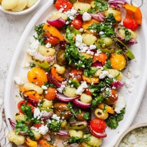 A white platter with vegetable and gnocchi skewers, topped with chopped herbs and crumbled cheese, is pictured next to small bowls of cooked gnocchi and crumbled cheese.