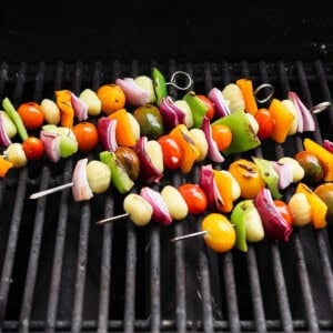 Vegetable skewers with tomatoes, onions, bell peppers, and gnocchi are grilling on a barbecue grate.